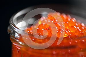 Red caviar in a glass jar, close up. Salmon caviar isolated on black background. Delicious gourmet food