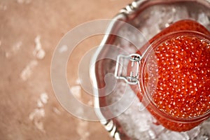 Red caviar in a glass jar with a yoke in a vintage metal dish filled with crushed ice with a curly spoon lying next to