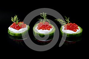 Red caviar on a green cucumber, over black