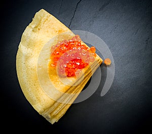 Red caviar on pancakes stack on black