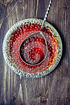 Red caviar in silver plate with spoon on wooden table.
