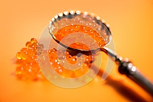 Red Caviar in a spoon. Caviar over orange background. Fish roe, Close-up salmon or trout caviar. Delicatessen