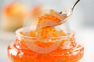 Red Caviar in a spoon, fish roe in a glass jar. Close-up of salmon fish roe caviar on served table