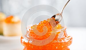 Red Caviar in a spoon, fish roe in a glass jar. Close-up of salmon fish roe caviar on served table