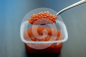 Red Caviar in a spoon and in plastic container over dark background. Close-up salmon caviar. Delicatessen. Seafood