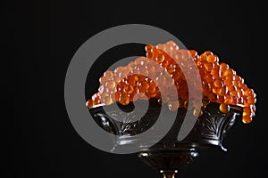 Red caviar in a vase on a black background. Salmon roe. A delicacy. A useful omega. Copy space.