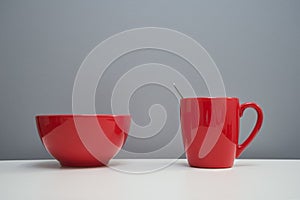 Red ceramic bowl and mug or cup for food and drink on white kitchen table with gray background