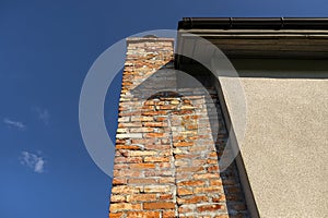 A red ceramic brick chimney standing at the rear of the building, by the facade, with a blue sky in the background.