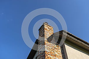 A red ceramic brick chimney standing at the rear of the building, by the facade, with a blue sky in the background.