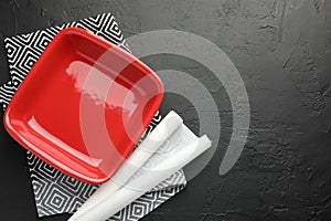 Red ceramic casserole and baking parchment paper on black table, top view. Space for text