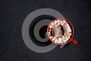 Red ceramic cups of hot cocoa with marshmallows on top of black rustic background