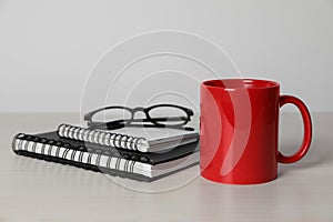 Red ceramic mug, stationery and glasses on white wooden table