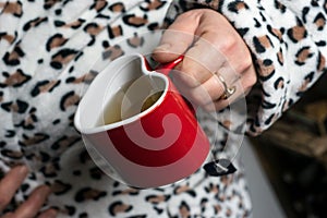 red ceramic mug of tea in shaped heart in hand of woman