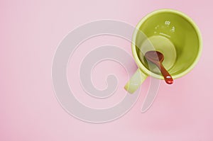 Red ceramic spoon in a light green mug on a light pink background