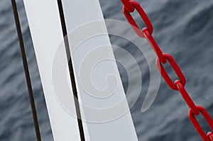 Red chain of anchor hanging on water, against sea