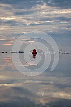 Red channel marker sticking out of a tranquil sea with the reflection of clouds on it at sunset