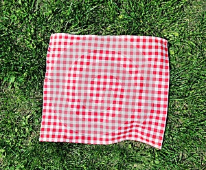 Red checkered cloth on green grass top view.