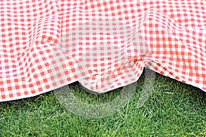 Red checkered picnic cloth on green grass background,empty space food advertisement backdrop