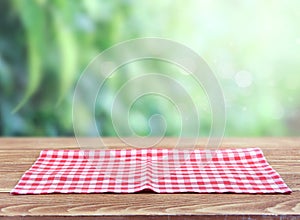 Red checkered picnic cloth on wooden tablue blurred green background