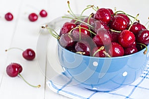 Red cherries in bowl on white wooden background on blue towel