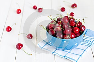 Red cherries in bowl on white wooden background on blue towel