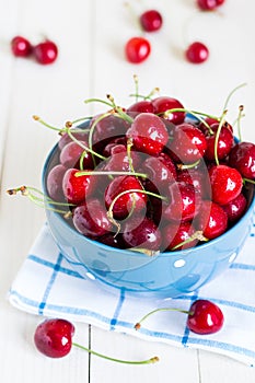 Red cherries in bowl on white wooden background on blue towel