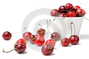 Red cherries in a ceramic bowl, scattering of berries, white background, close-up