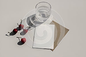 Red cherries fruit on beige table background. Stationery mock up. Blank greeting card, invitation with craft envelope