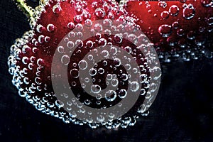 Red cherries in a mineral water with lots of bubbles on a black background, close up