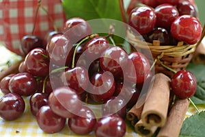 Red cherries with stems and cinnamon rods in front of litlle basket