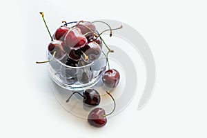 Red cherries in transparent glass bowl on light background.