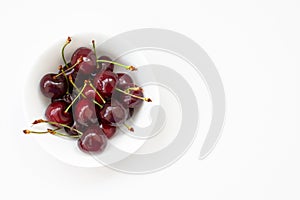 Red cherries in a white bowl on the white background, isolated.