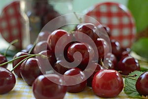 Red cherries on yellow tablecloth and red cap of jars