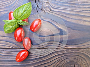 Red cherry tomatoes and basil leaves on a wooden background. Selective focus. Local products consumption concept. Healthy eating