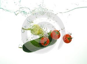 Red cherry tomatoes cucumber and green papper under water spash on white background