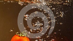 Red cherry tomatoes falling into water with air bubbles. Black background. Slow motion