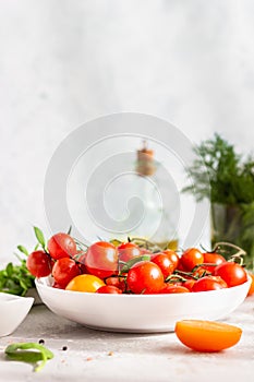 Red cherry and yellow tomatoes on the white plate, olive oil and dill. Low-calorie dietary food concept