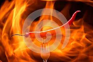 red chili pepper, pricked on a fork, on a background of burning fire, flames on a black background photo