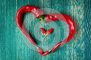 Red chili peppers in heart shape on green wooden backhround, indicating hot love for valentine's day