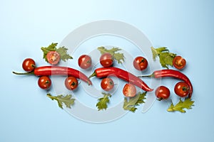 Red chili peppers, tomatoes and green rucola salad leaves on blue background