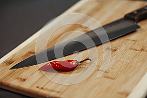 Red Chilli on the old wooden chopping board and shiny knife next to them