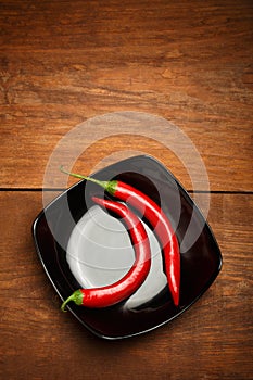 Red chilli peppers on black ceramic plate standing on brown wood
