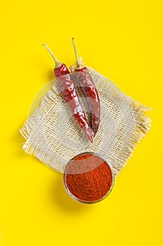 Red chilli powder in glass bowl on yellow background. top view