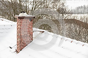 Red chimney and roof covered with snow