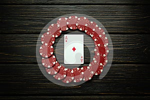 Red chips and ace of diamonds playing card on a black vintage table. Low key concept of luck or winning in poker club