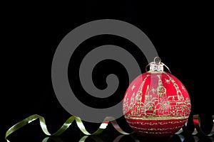 Red Christmas ball with a golden painting of the old city and a golden ribbon on a black background.