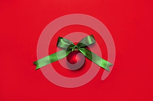 Red Christmas ball with green ribbon on red background Flat lay top view copy space. Christmas winter decoration Xmas holiday. Con