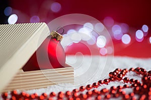 Red Christmas ball in open box with beads and garland lights on bokeh background