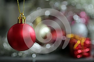 Red Christmas ball ornament hanging on a blur tree bokeh light festive background.