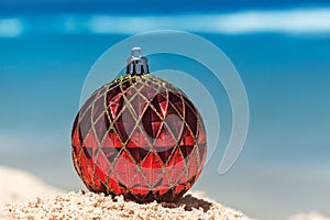 Red Christmas ball on sandy tropical beach, holiday concept